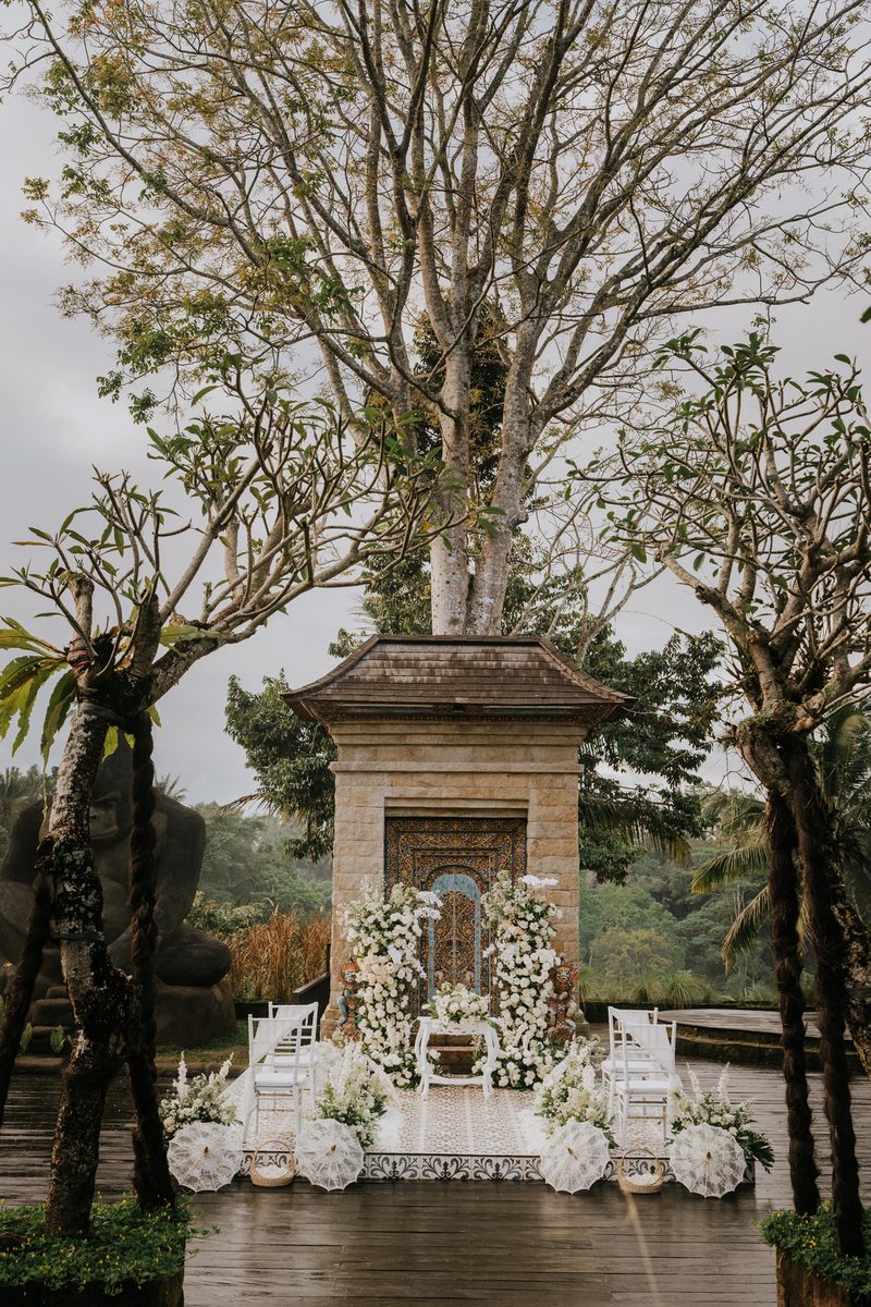 Ceremony aisle with white chairs and flowers before a stone gate